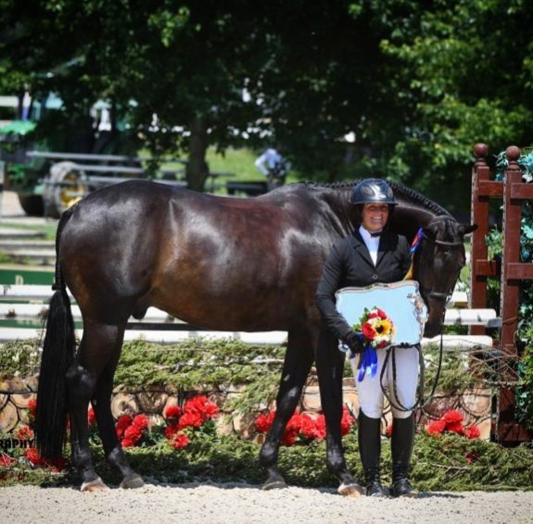 A person standing next to a horse in front of some flowers.